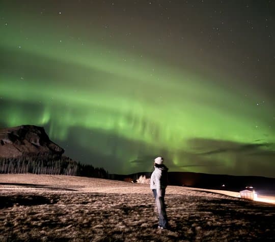 A figure standing under green northern lights in Iceland